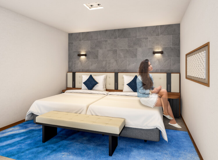 ホテルのベッドルームで、白と青を基調にしたインテリアデザイン。壁にグレーのアクセントがあり、女性がベッドの端に座っている。