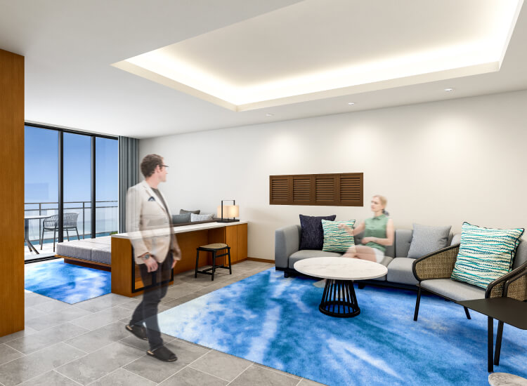 開放感のあるリビングスペースで、男性が立ちながら女性と会話している。青いラグとナチュラルウッドの家具が温かみを演出。