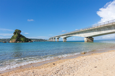 古宇利ビーチの穏やかな海岸線。手前には白い砂浜と波打ち際が広がり、その向こうには透き通ったエメラルドグリーンの海が続く。