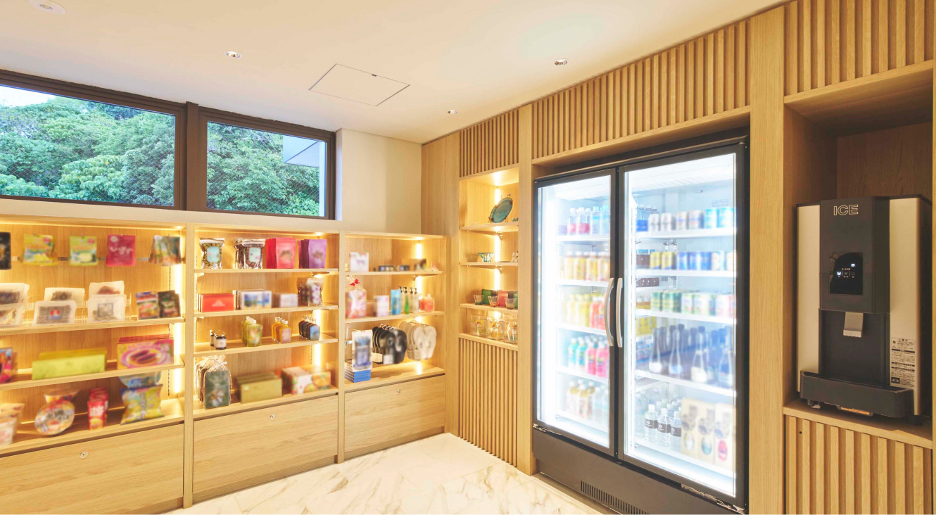 木目調の棚と白い壁で構成された明るいショップの店内。左手には壁一面に商品が並べられた木製の棚が複数あり、様々なパッケージのお菓子や小物、お土産品などがディスプレイされている。